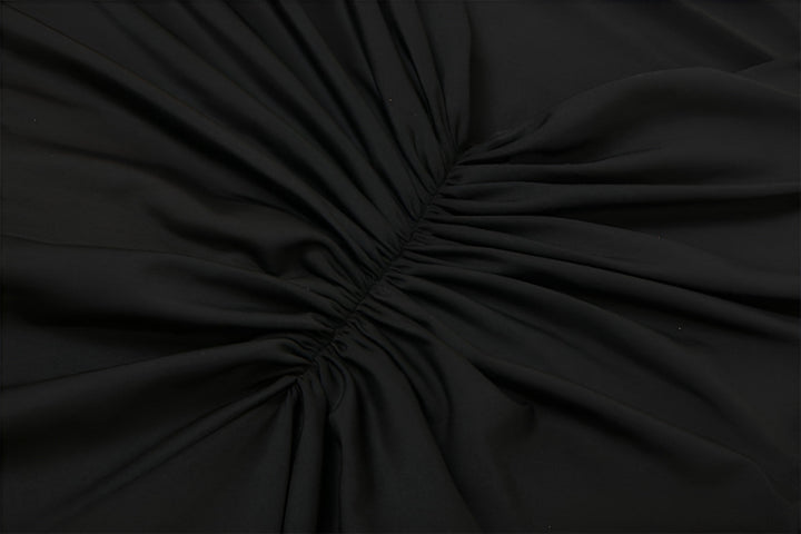 Wrinkled black fabric with radiating folds converging at a central point.